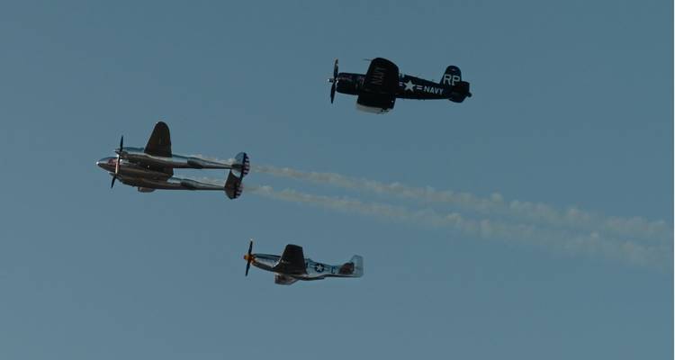 Trío de aviones históricos volando en formación con débiles rastros de humo en un día sin nubes.