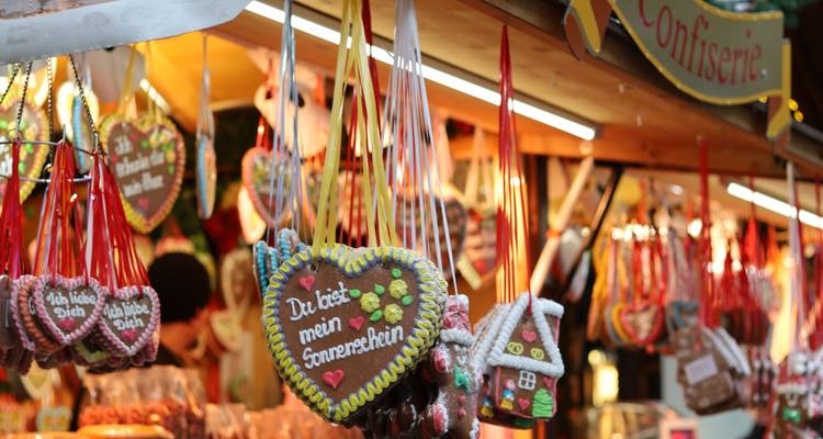 Gros plan de biscuits au pain d'épices en forme de cœur suspendus avec des inscriptions allemandes à un étalage du marché de Noël festif.