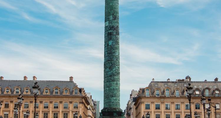 La Colonne Vendôme s'élevant entre d'élégants bâtiments parisiens sous un ciel bleu dégagé.