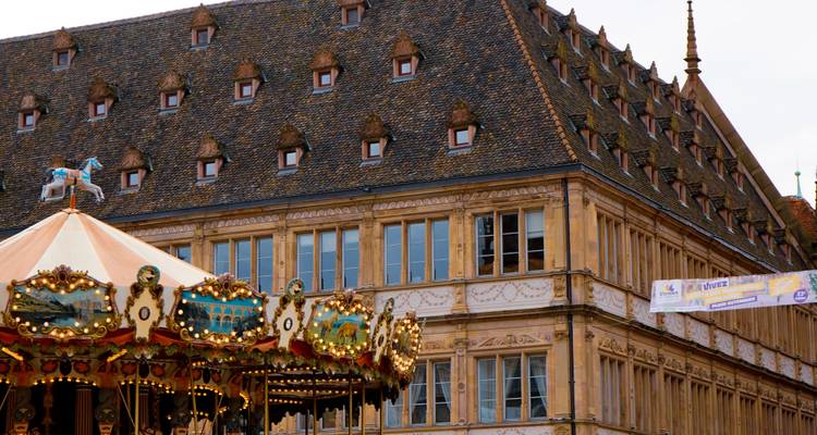 Carrousel vintage aux chevaux ornementés tournoyant devant un bâtiment historique de Strasbourg aux toits en bois.