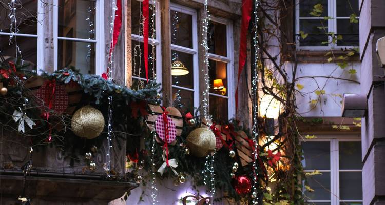 Les vitrines festives d'un ancien bâtiment européen ornées de guirlandes de Noël, de boules décoratives et de guirlandes lumineuses scintillantes.