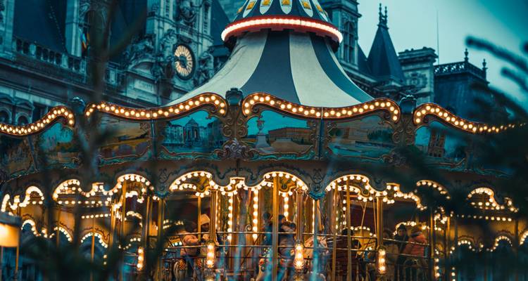 Carrousel vintage illuminé tournoyant devant un bâtiment d'hôtel de ville orné pendant le crépuscule.