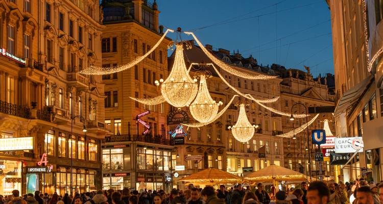 Rue commerçante viennoise bondée la nuit avec des lustres de Noël ornementés suspendus au-dessus.