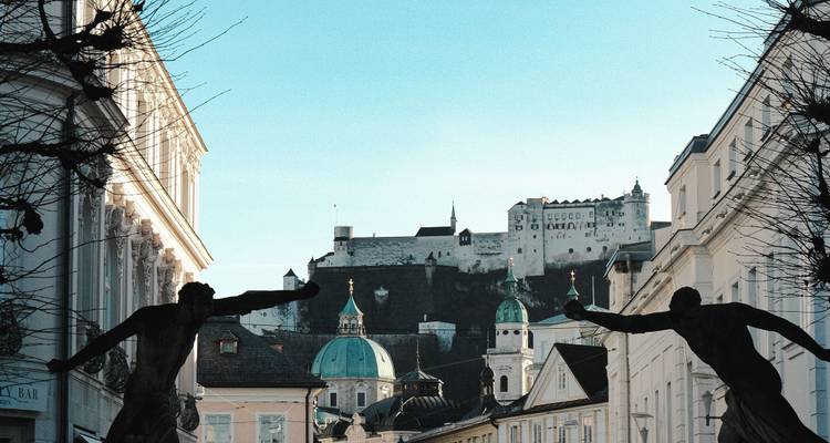 La vieille ville de Salzbourg encadrée par des statues avec la forteresse de Hohensalzburg dominant l'horizon lors d'une matinée dégagée.
