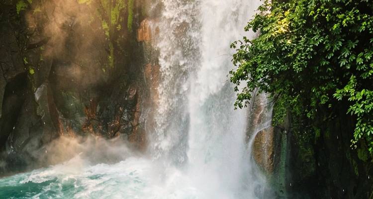 Una poderosa cascada que se lanza en picada en una piscina turquesa rodeada de exuberante vegetación.