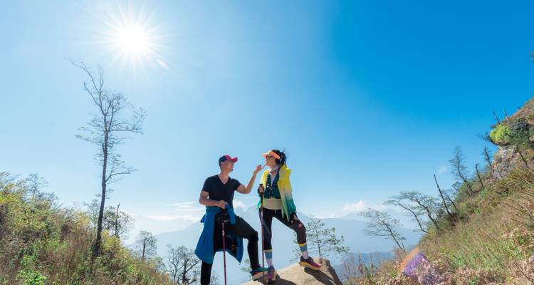 Couple souriant échangeant un high-five sur un affleurement rocheux sous un ciel bleu dégagé