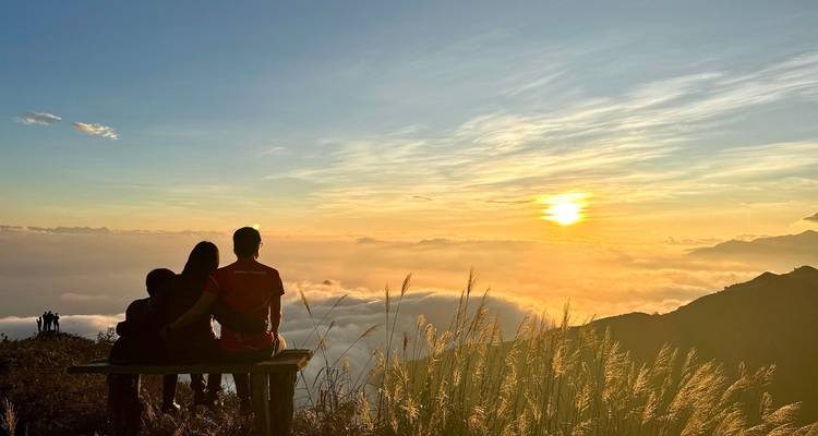 Famille assise sur un banc regardant un coucher de soleil doré au-dessus d'une inversion de nuages et de montagnes