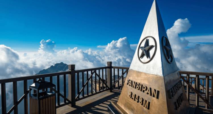Pyramide emblématique du sommet de Fansipan sur une plateforme d'observation en bois entourée de nuages dramatiques et de ciel bleu.