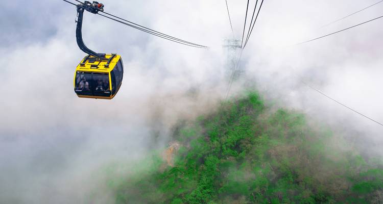 Une cabine de téléphérique jaune vif glisse à travers un épais brouillard au-dessus d'un versant montagneux luxuriant et verdoyant.