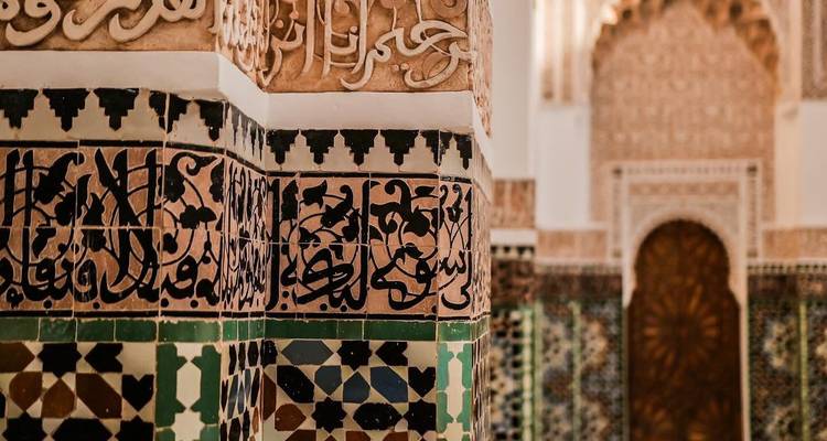 Gros plan sur la calligraphie arabe complexe et les carreaux de mosaïque colorés à l'intérieur d'une madrasa marocaine.