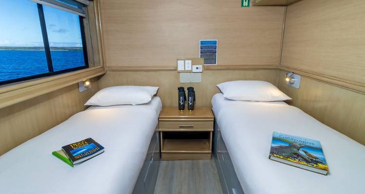 Cabine double sur le yacht avec vue sur la mer par le hublot, des jumelles et des guides de voyage sur les lits.