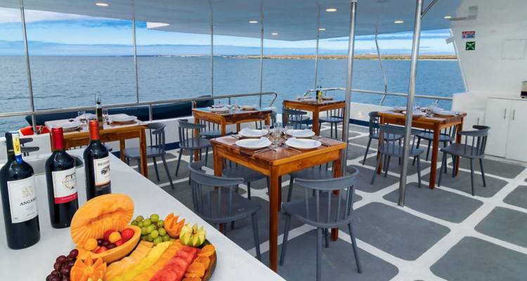 Espace de restauration en plein air sur un yacht avec un plateau de fruits, du vin et l'horizon marin en arrière-plan.