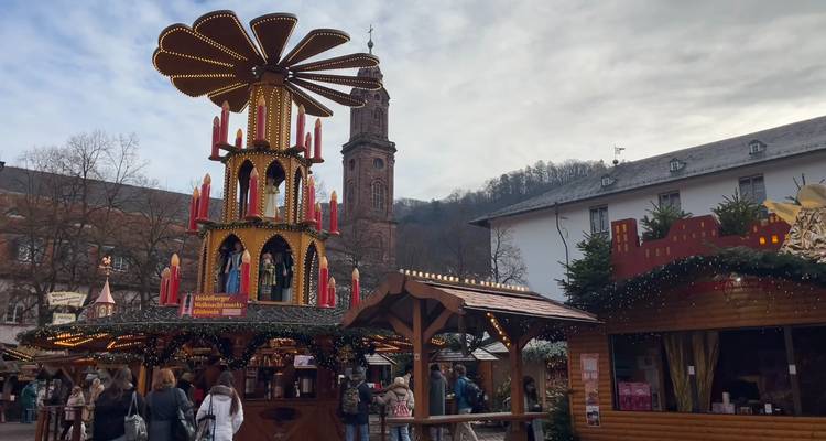Tour pyramidale de Noël illuminée de grande hauteur au marché festif avec le clocher de l'église en arrière-plan.