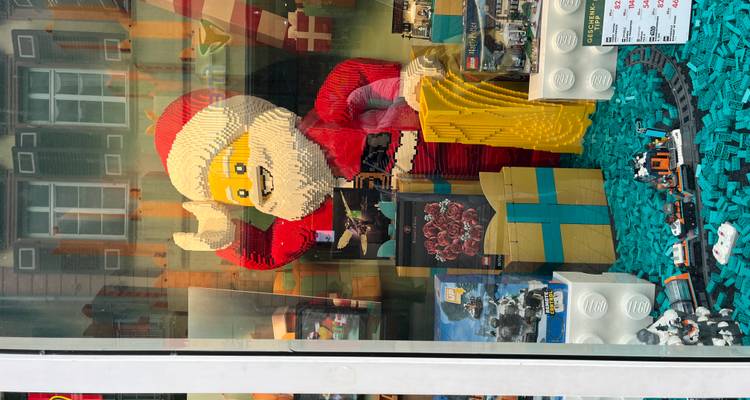Vitrine de magasin présentant une grande figurine LEGO du Père Noël entourée d'ensembles emballés.