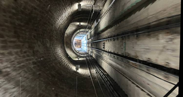 Vue dans un tunnel de funiculaire faiblement éclairé avec des voies ferrées jumelées s'étendant au loin.