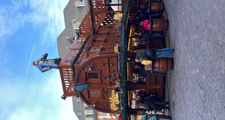 Taverne du marché de Noël en bois à deux étages décorée de guirlandes tandis que les visiteurs se rassemblent en dessous.