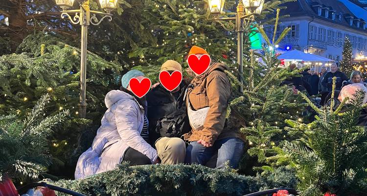 Trois visiteurs bien emmitouflés assis dans un traîneau festif entouré de verdure de Noël ; les visages couverts de graphiques en forme de cœur.