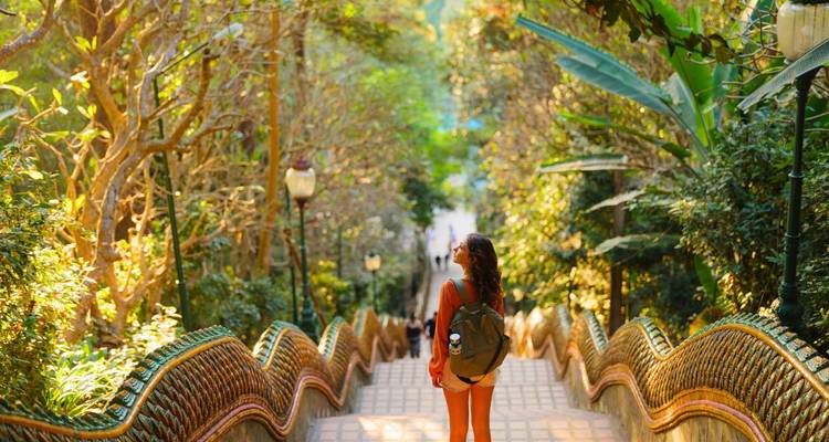 Vue arrière d'une femme descendant l'escalier orné des Nagas à travers la jungle luxuriante du Wat Phra That Doi Suthep.
