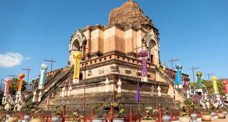 Stupa en brique du Wat Chedi Luang orné de drapeaux festifs colorés sous un ciel dégagé.
