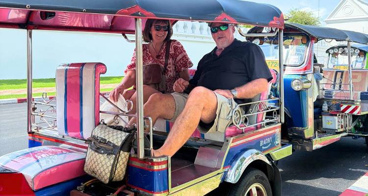 Un couple de touristes roule dans un tuk-tuk aux couleurs vives dans une rue de Bangkok.