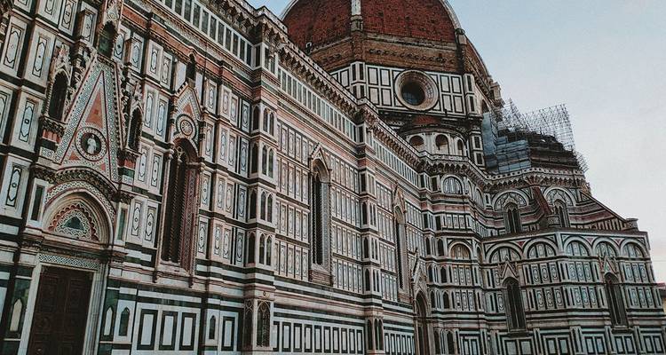 Vue rapprochée de la façade de la cathédrale de Florence, mettant en évidence les motifs complexes de marbre vert, blanc et rose sous le dôme rouge.