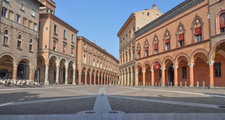 Une piazza médiévale vide à Bologne encadrée par d'élégantes galeries couvertes et des bâtiments en terre cuite lors d'une matinée dégagée.