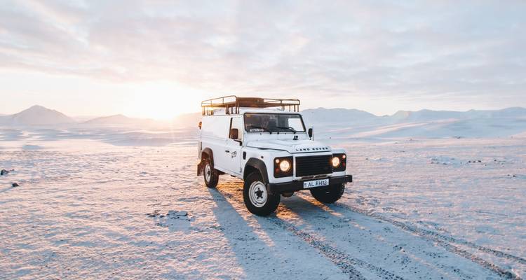 Un robuste Land Rover 4x4 se dresse seul sur une vaste plaine glacée baignée de la douce lumière de l'aurore arctique.