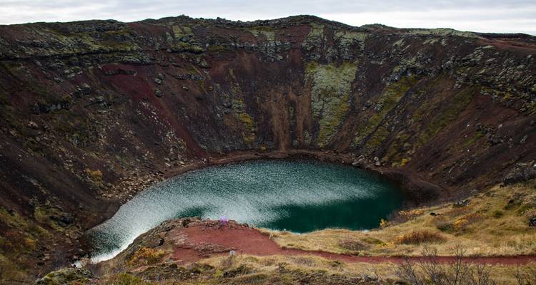 Le lac de cratère volcanique circulaire de Kerid brille d'une teinte turquoise au milieu de pentes rouges et vertes striées de mousse.