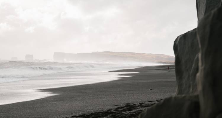 La brume s'élève au-dessus de la plage sauvage aux sables noirs près de Dyrhólaey tandis que les vagues se brisent sous un ciel chargé.