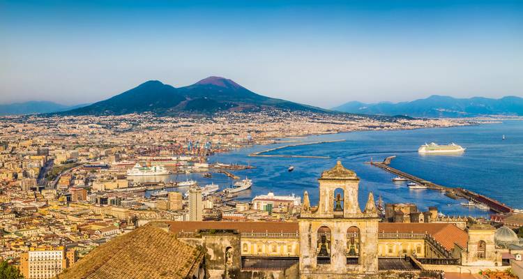 Vue panoramique sur Naples avec le Mont Vésuve dominant au-delà de la ville et la Baie de Naples par une journée dégagée.