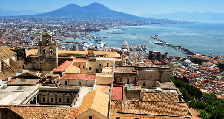 Point de vue élevé du port de Naples avec des navires de croisière et le Mont Vésuve en arrière-plan sous un ciel bleu brumeux.