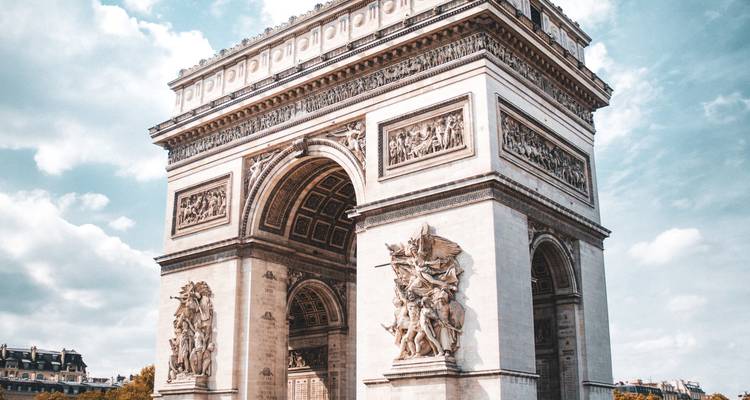 Arc de Triomphe brillamment illuminé contre un ciel partiellement nuageux, vue du niveau du sol.