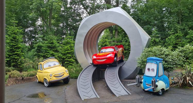 Attraction sur le thème des Voitures avec trois véhicules de dessins animés sur un circuit automobile situé dans un cadre verdoyant.