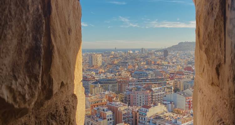 Vue panoramique de la skyline de Barcelone aperçue à travers une ouverture de fenêtre en pierre, dominant les toits de la ville.