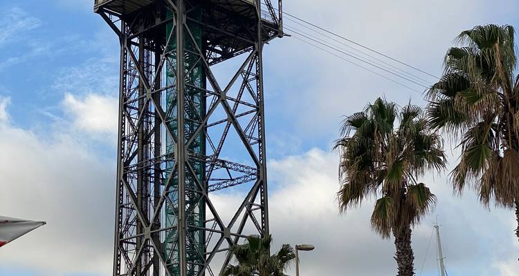 Grande tour de téléphérique en acier s'élevant à côté de palmiers oscillants sous un ciel partiellement nuageux.