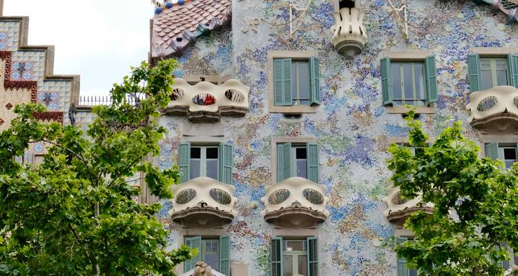 Façade en mosaïque colorée de la Casa Batlló avec des balcons organiques partiellement encadrés par des arbres verts.