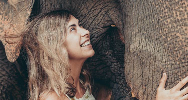 Close-up of a smiling woman pressing her face to an elephant’s head, capturing an intimate moment.
