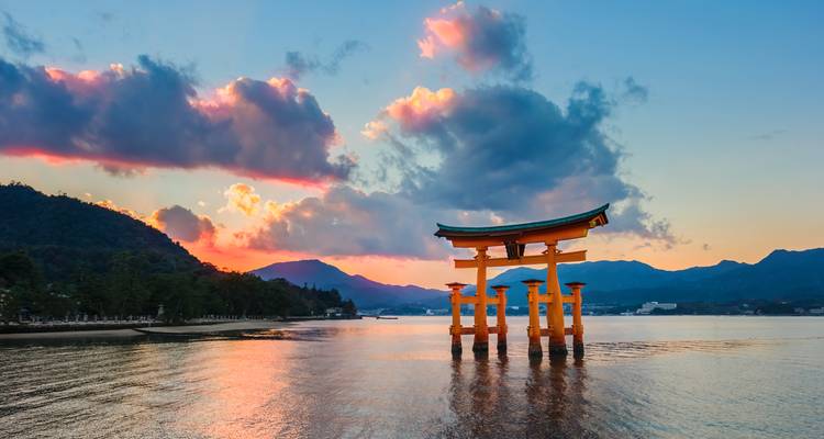 Icónica puerta torii flotante del Santuario Itsukushima al atardecer reflejándose en aguas tranquilas.