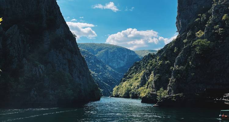 Paredes de cañón empinadas y la vía acuática de esmeralda tranquila del Cañón de Matka bajo un cielo brillante