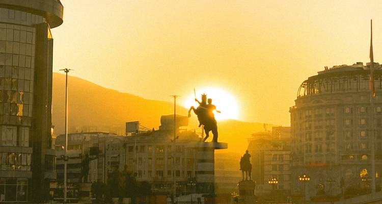 Silueta de la estatua de Alejandro Magno contra la salida del sol dorada sobre el horizonte de la ciudad de Skopje