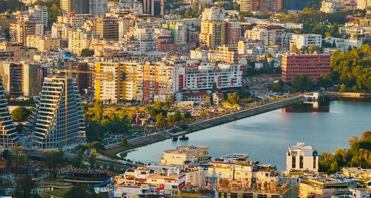 Vista aérea del atardecer sobre el paisaje urbano de Tirana con frente al lago y edificios modernos