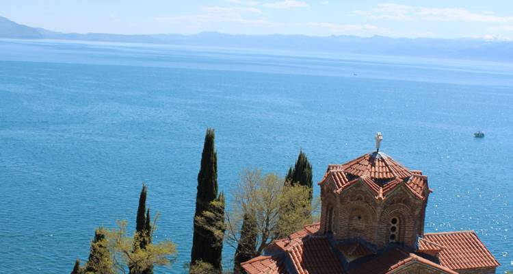 Aguas azules del Lago Ohrid con la Iglesia de San Juan en Kaneo, con techo de tejas, encaramada en la orilla