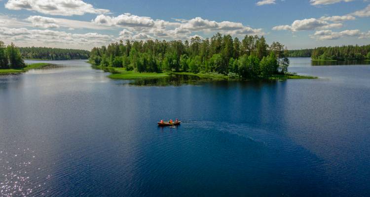 Una canoa roja sola con dos remeros a la deriva en un lago tranquilo y enorme rodeado de bosque verde exuberante.