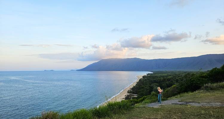 Voyageur solo appréciant une vue côtière panoramique au crépuscule avec une longue plage de sable et des îles lointaines.