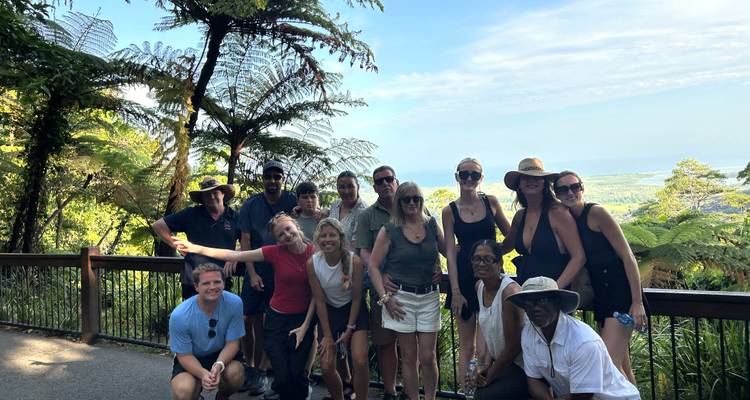 Groupe de touristes souriants posant sur une plateforme d'observation entourée d'une forêt tropicale luxuriante avec des vues côtières au-delà