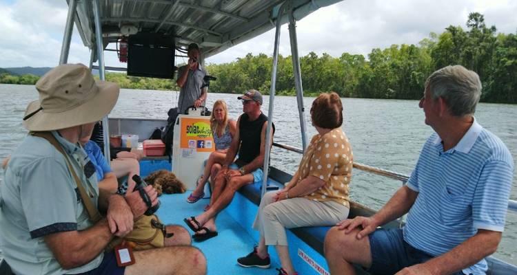 Un petit groupe est assis à bord d'un bateau de visite ouvert qui navigue sur une rivière calme bordée d'une forêt tropicale dense.