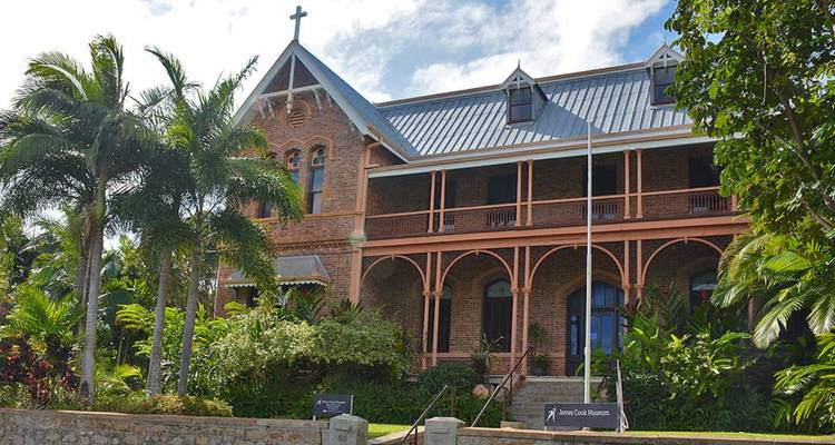 Edificio de museo colonial de ladrillo rojo enmarcado por palmeras y jardines exuberantes.