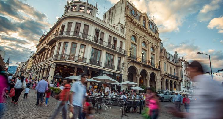 Busy plaza with historic architecture, outdoor cafés and blurred motion of city life at dusk.