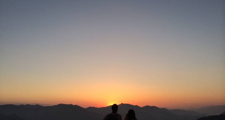 Silhouettes de deux personnes regardant le coucher de soleil sur les montagnes.