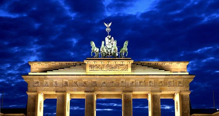 Brandenburger Tor bei Nacht beleuchtet mit dramatischem Himmel.